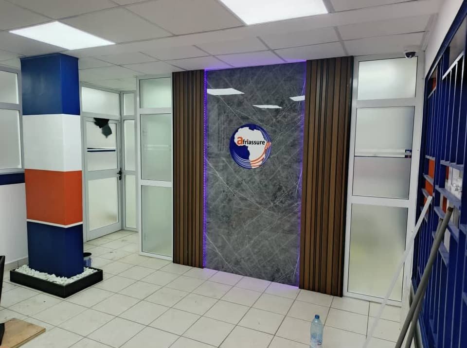 Intérieur d’agence : panneau mural au logo, cloisons vitrées et colonne bleu, blanc et orange