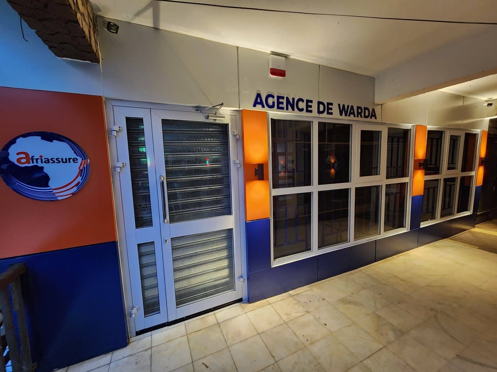 Façade d’agence bleu, orange et blanc avec enseigne et portes vitrées